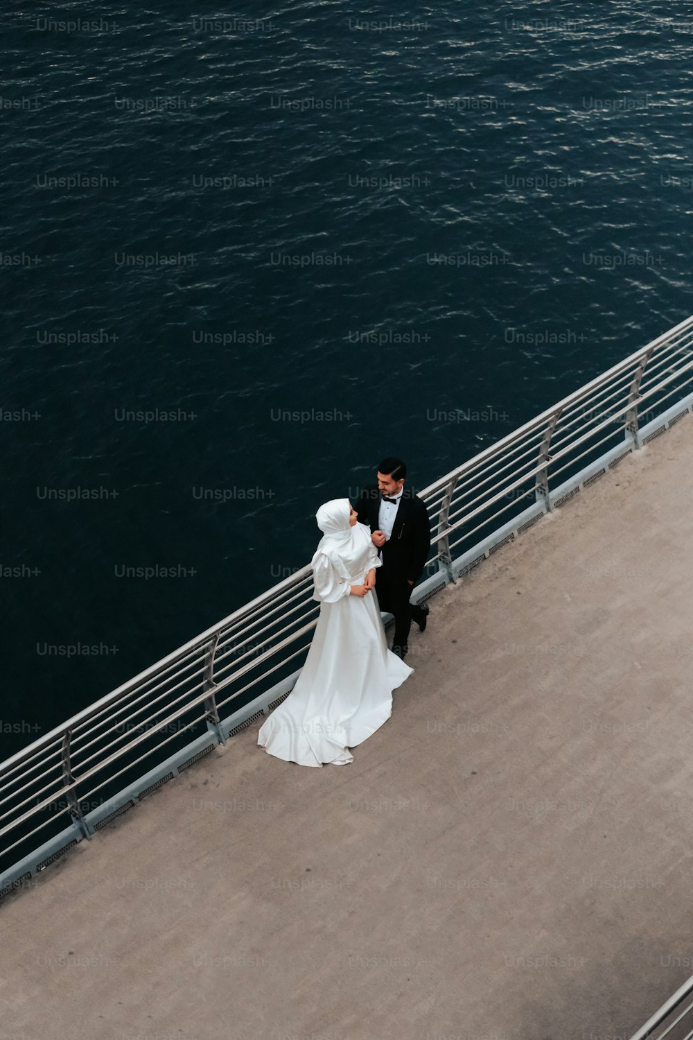 Una sposa e uno sposo in piedi su un molo accanto a uno specchio d'acqua