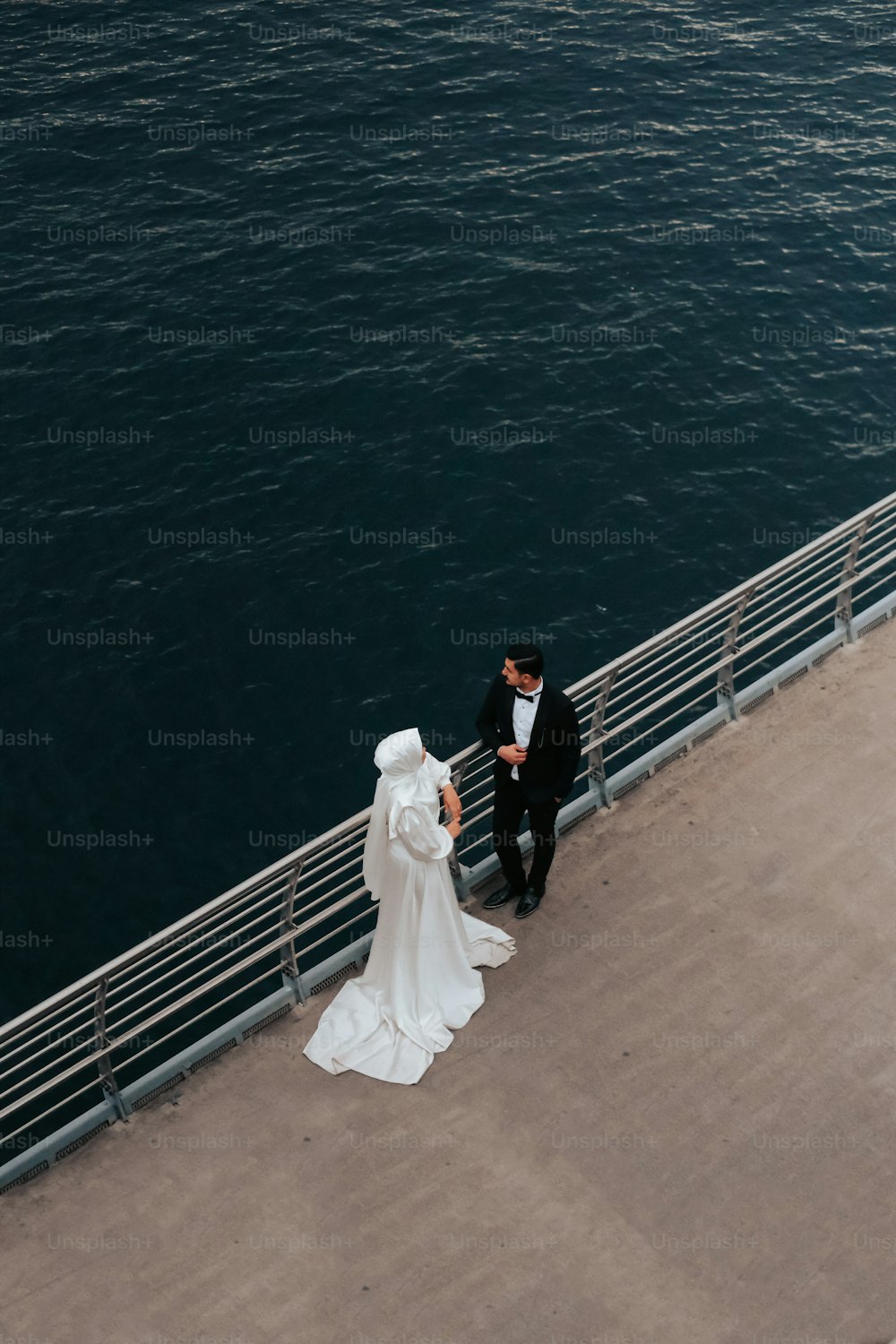 Una sposa e uno sposo in piedi su un molo vicino all'oceano
