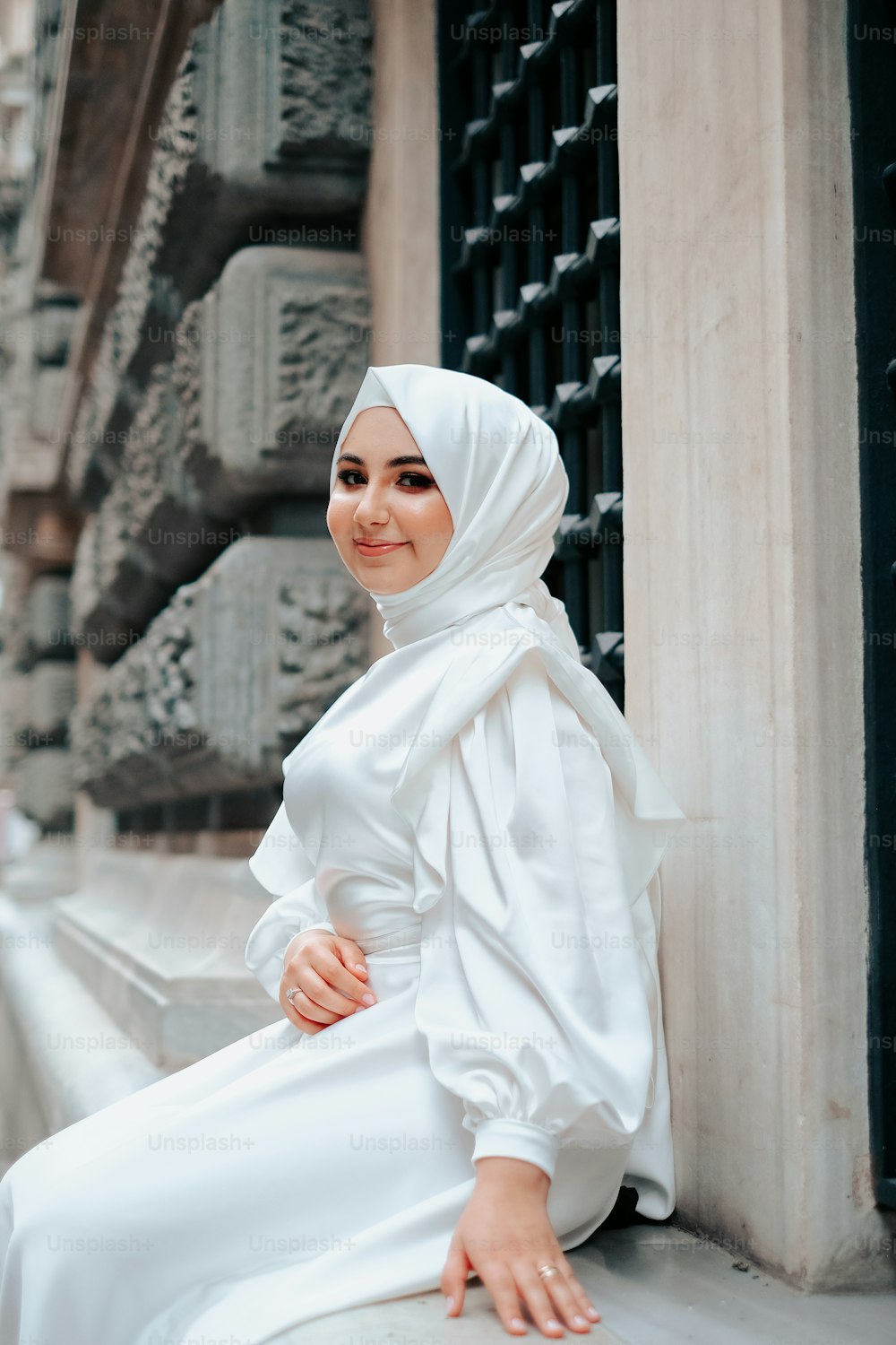 Una mujer con un hijab blanco sentada en una repisa