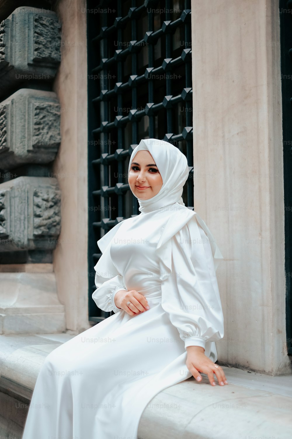 a woman in a white dress sitting on a ledge