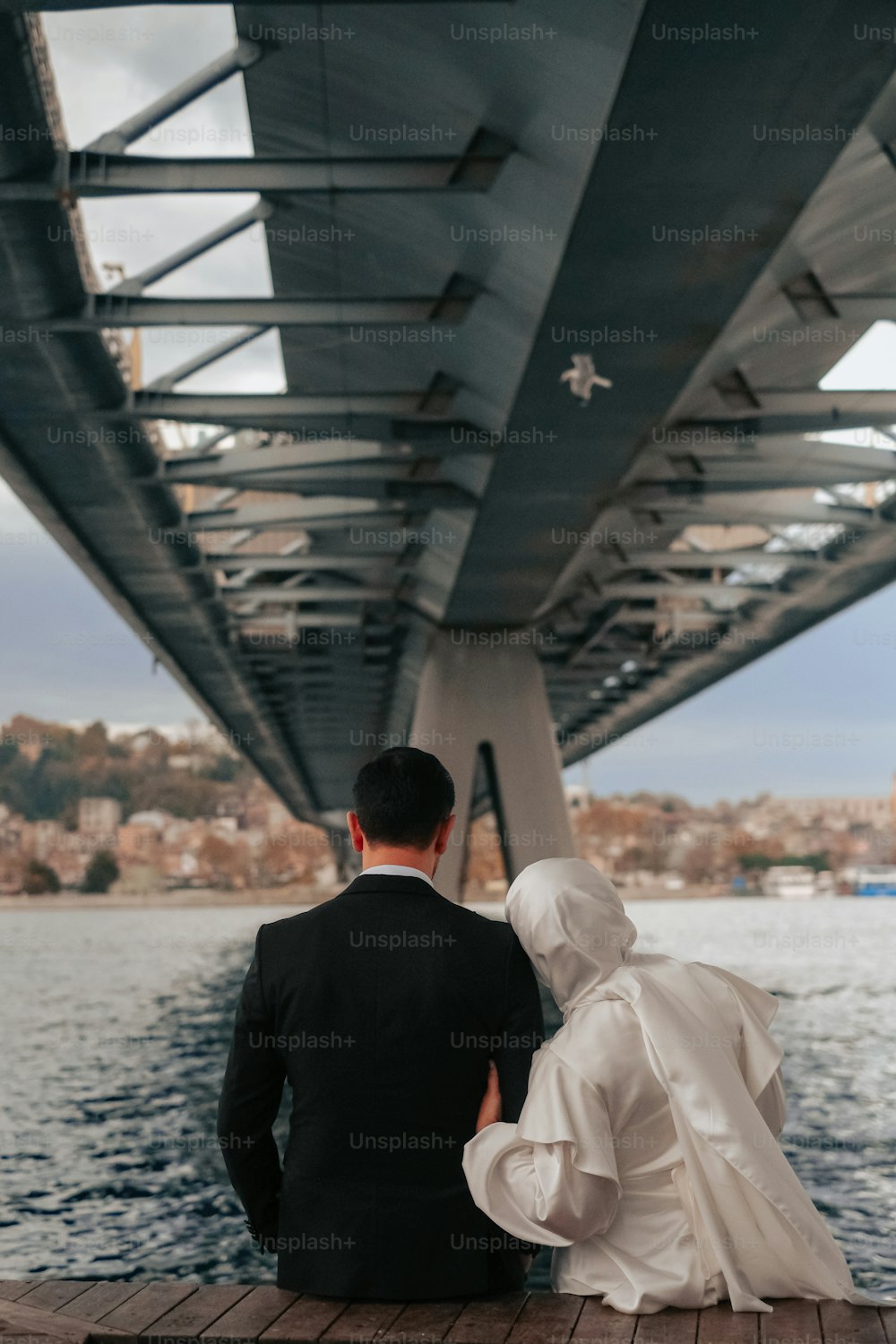 a bride and groom are sitting on a dock