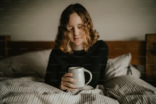 une personne assise sur un lit tenant une tasse de café