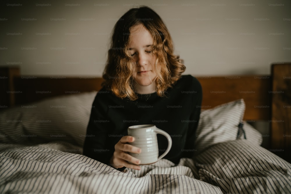 a person sitting on a bed holding a coffee cup