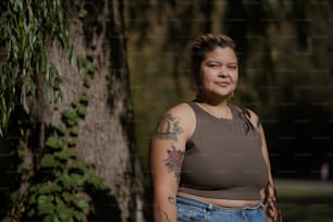 a woman with tattoos standing next to a tree