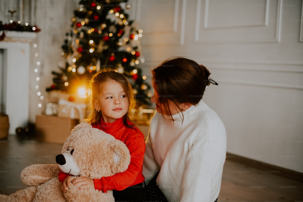a person and a girl holding a stuffed animal in front of a christmas tree