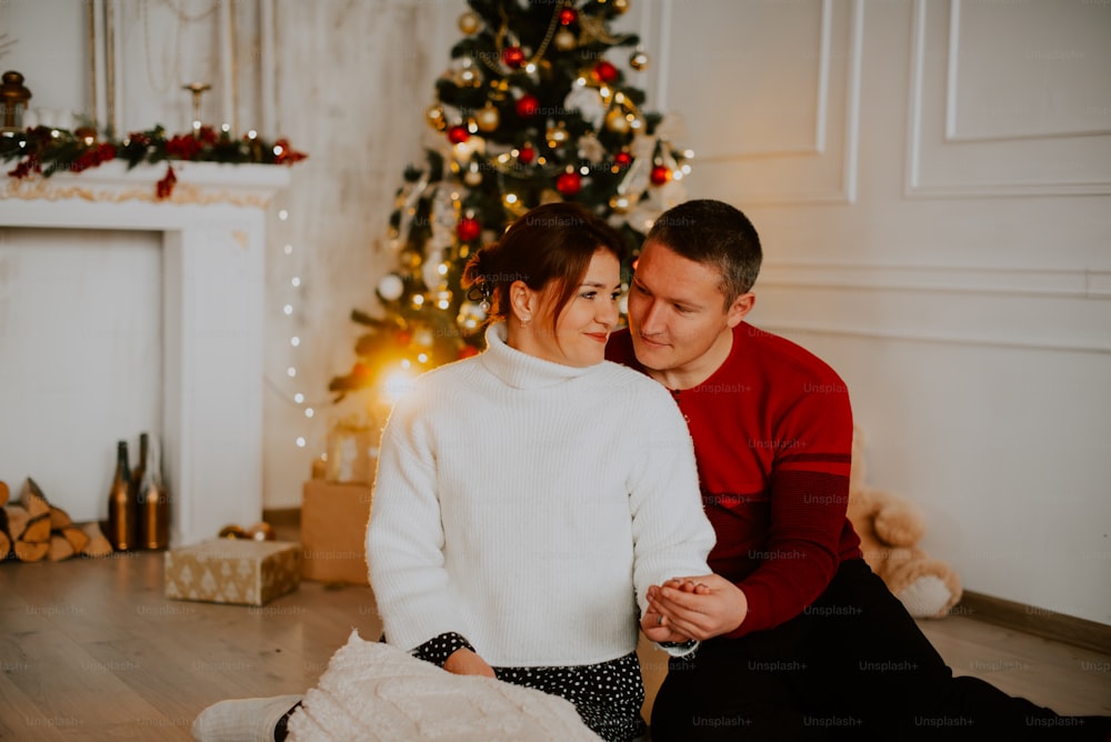 a man and woman sitting next to a christmas tree