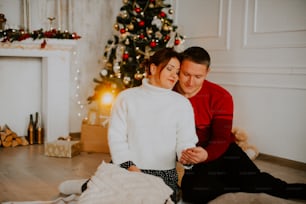 a man and woman sitting on the floor in front of a christmas tree
