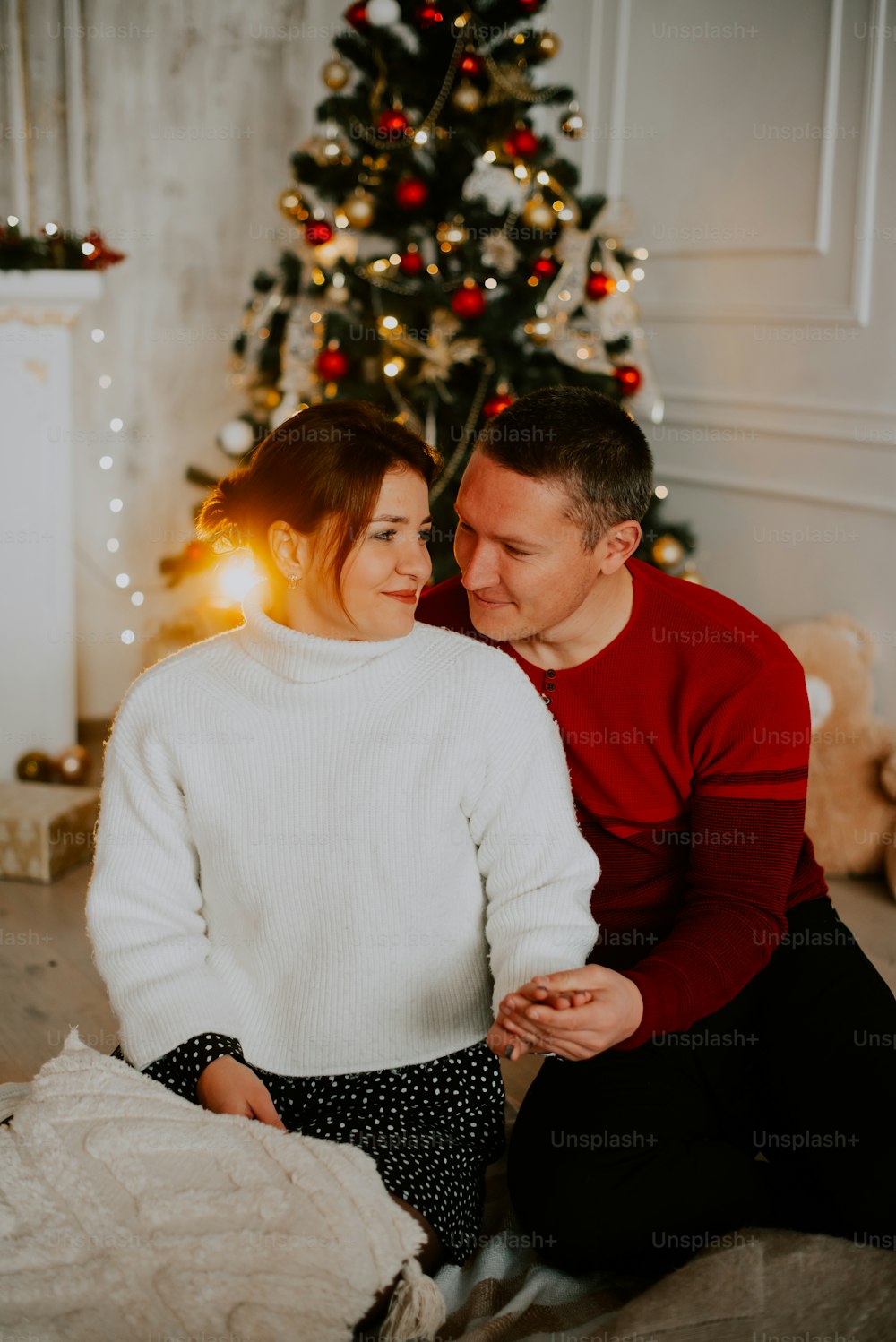 um homem e uma mulher sentados em um sofá na frente de uma árvore de Natal