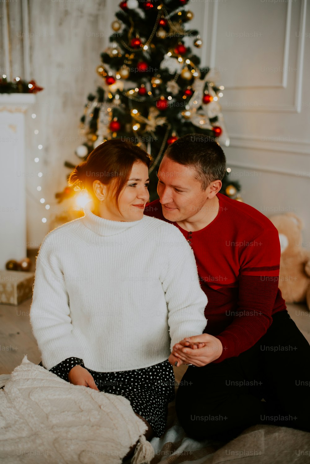 a man and woman sitting on a couch in front of a christmas tree