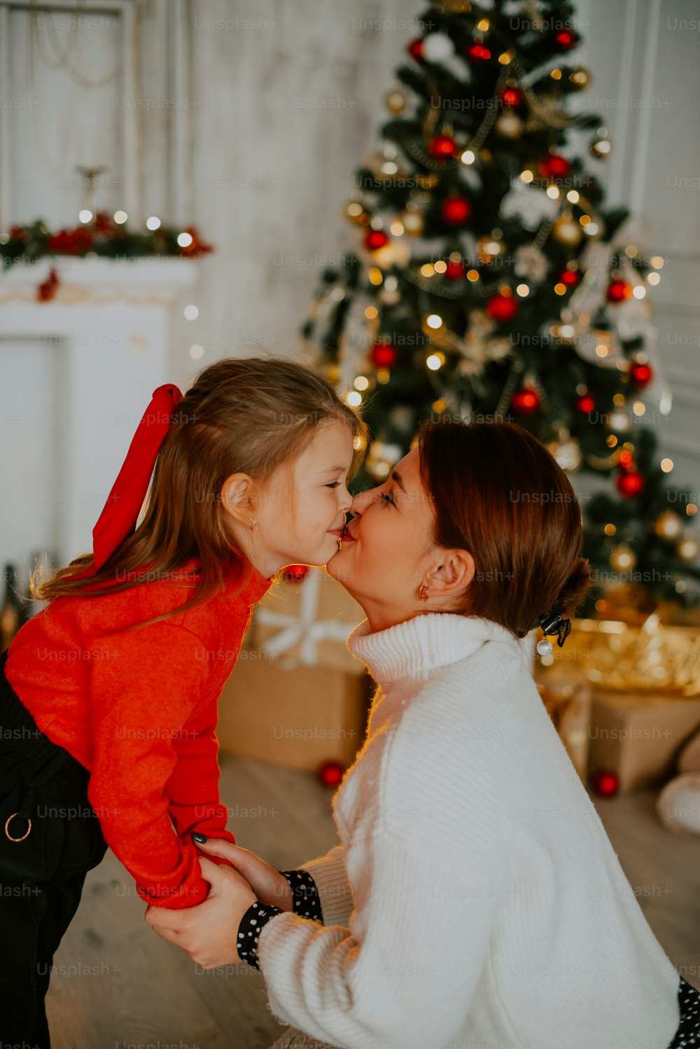 a person kissing a child in front of a christmas tree