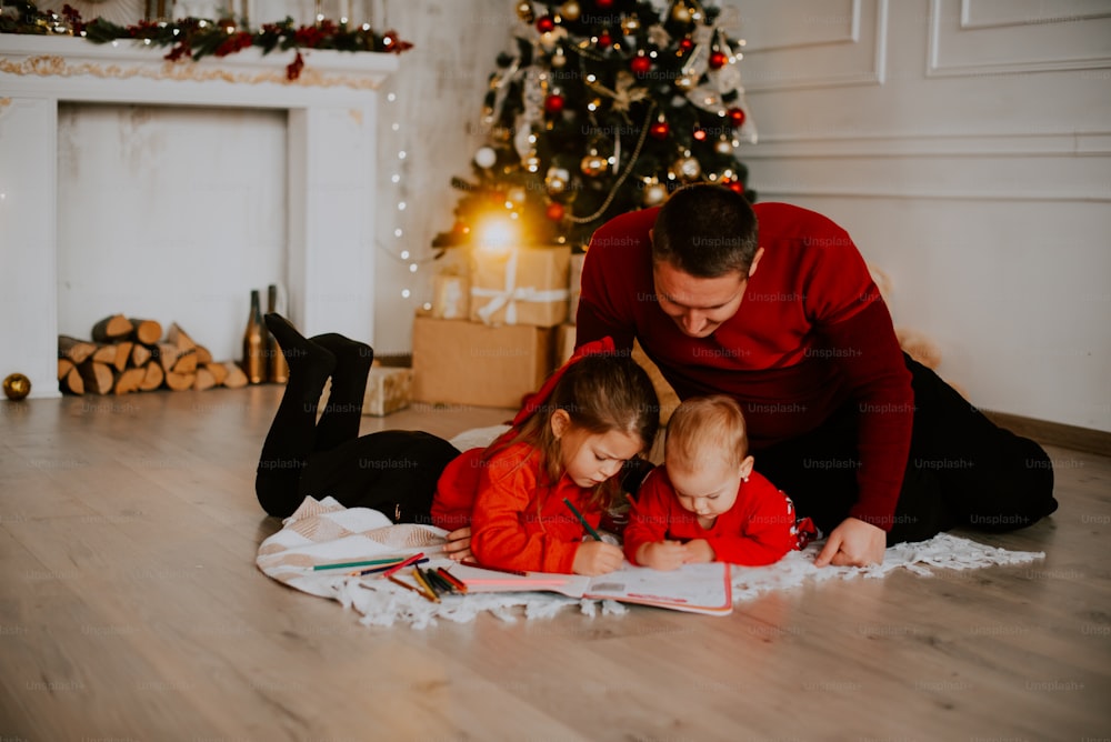 Una persona e due bambini seduti sul pavimento di fronte a un albero di Natale