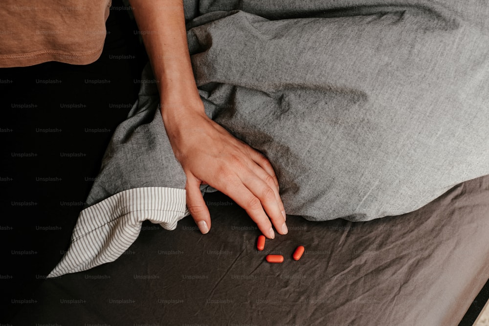 uma pessoa deitada em uma cama com pílulas na mão