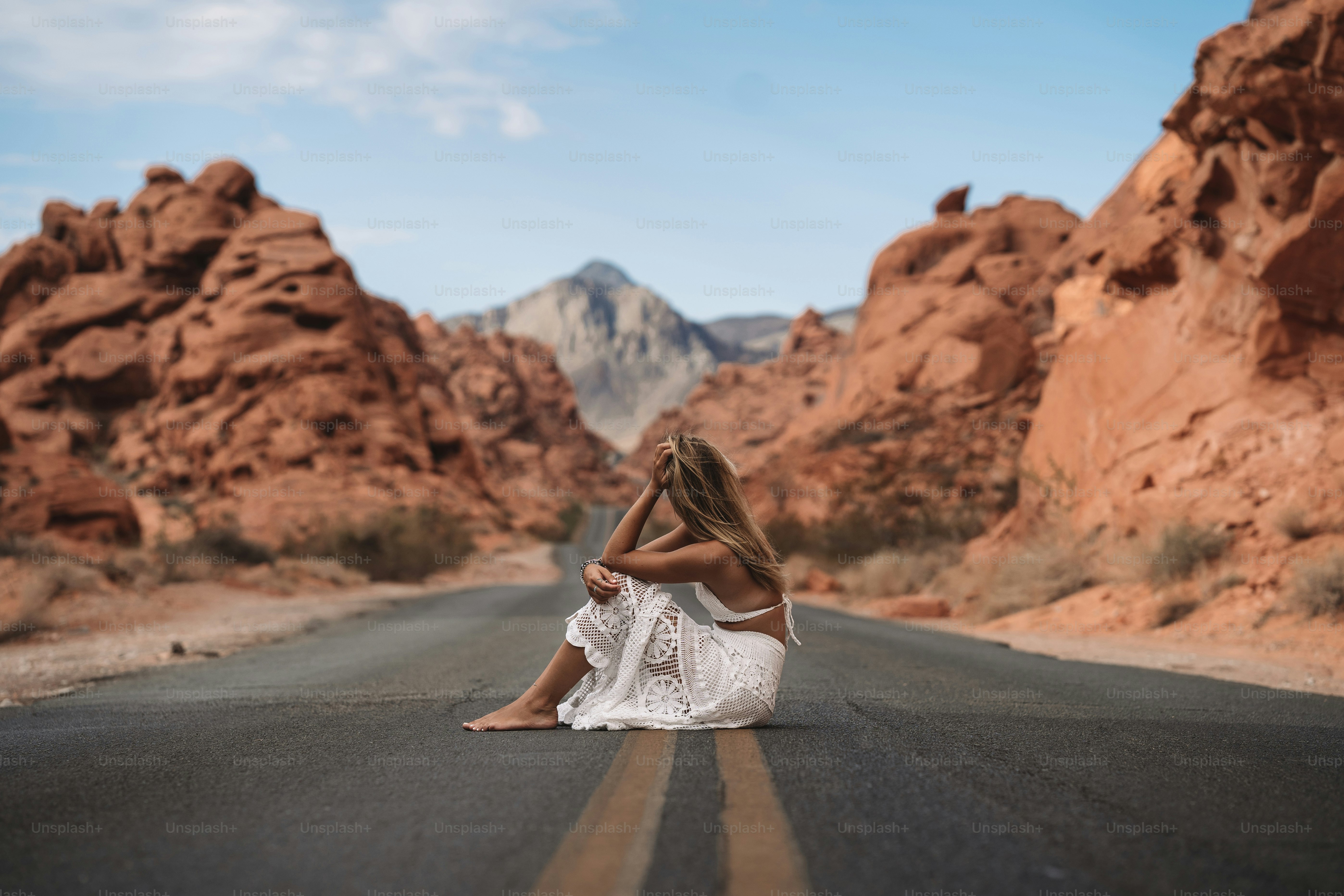 a person sitting on the side of a road in front of a rocky mountain