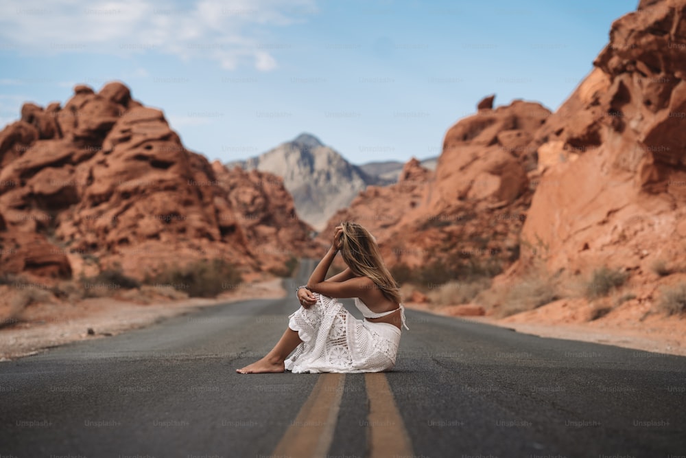 a person sitting on the side of a road in front of a rocky mountain