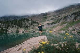 a person running on a trail by a lake with trees and mountains in the background