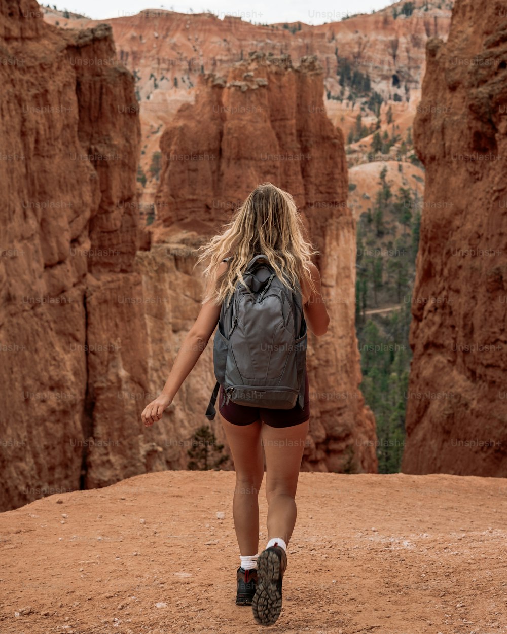 uma pessoa andando em um caminho de terra entre grandes formações rochosas vermelhas