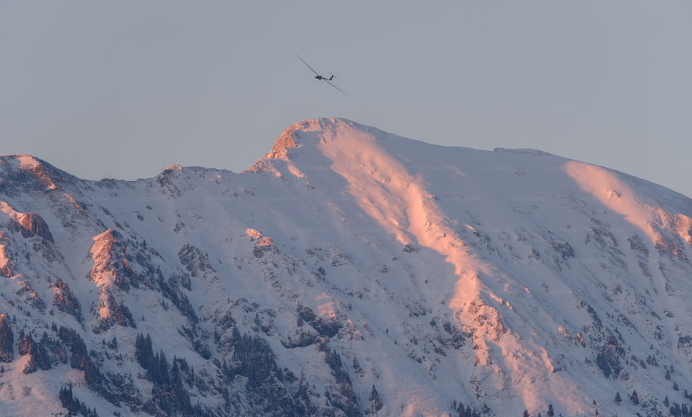 uma montanha nevada com um helicóptero voando sobre ela