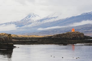 Ein kleiner orangefarbener Leuchtturm auf einer felsigen Insel vor einem Berg