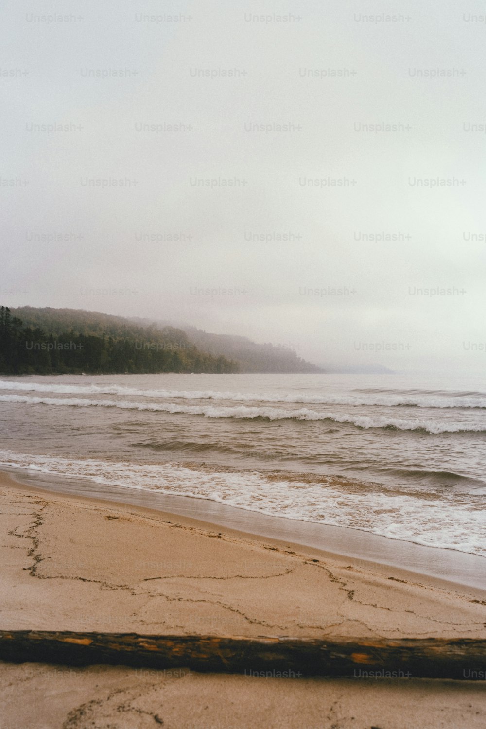 a beach with waves and a hill in the background