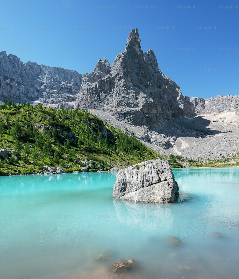a large rock in a body of water with mountains in the background