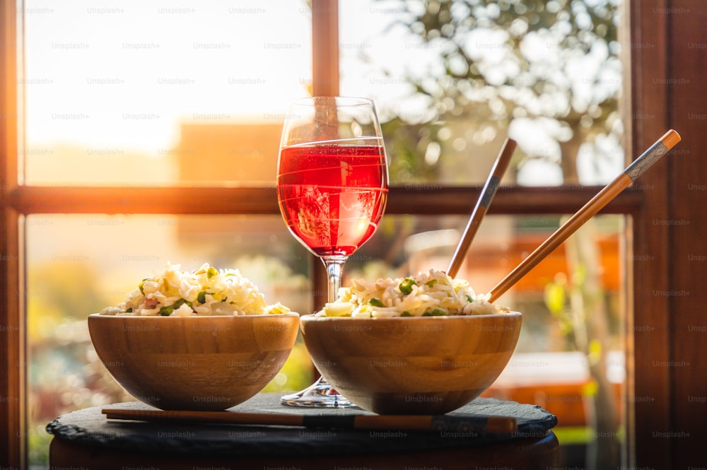 a glass of red wine next to a bowl of salad and a bowl of pasta