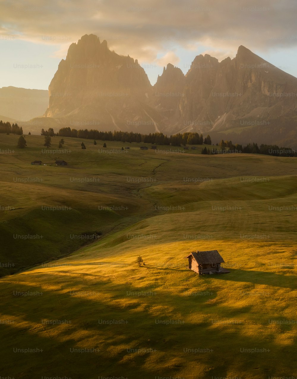 a grassy field with a few buildings and mountains in the background