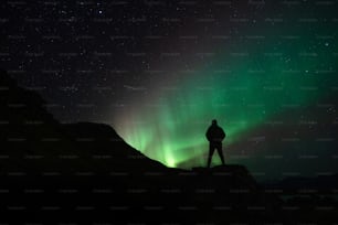 Eine Person, die auf einem Berg steht und auf das Nordlicht schaut