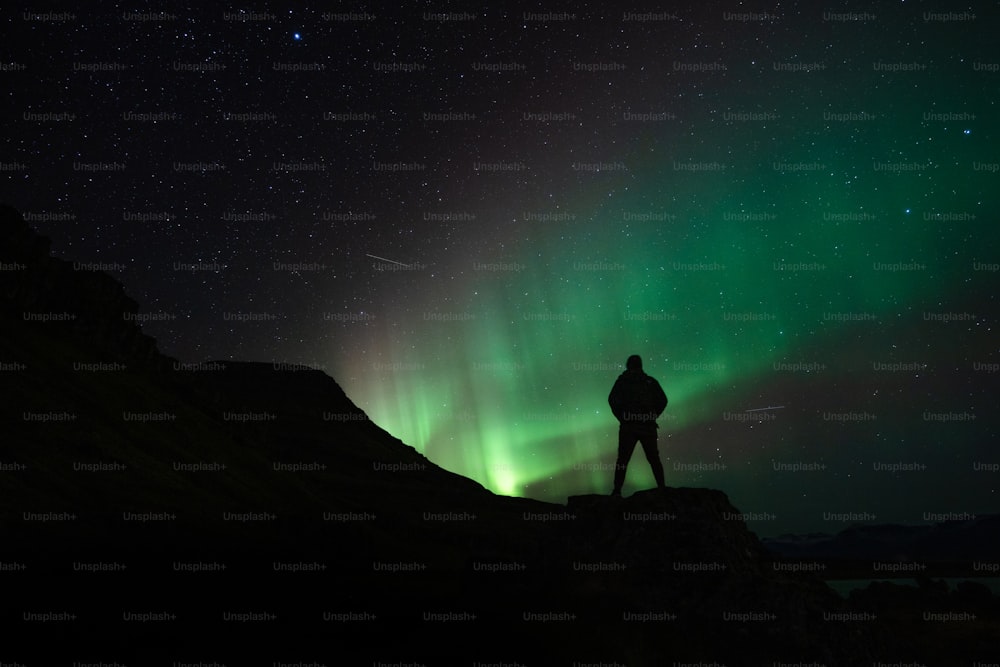 uma pessoa de pé em uma montanha olhando para as luzes do norte