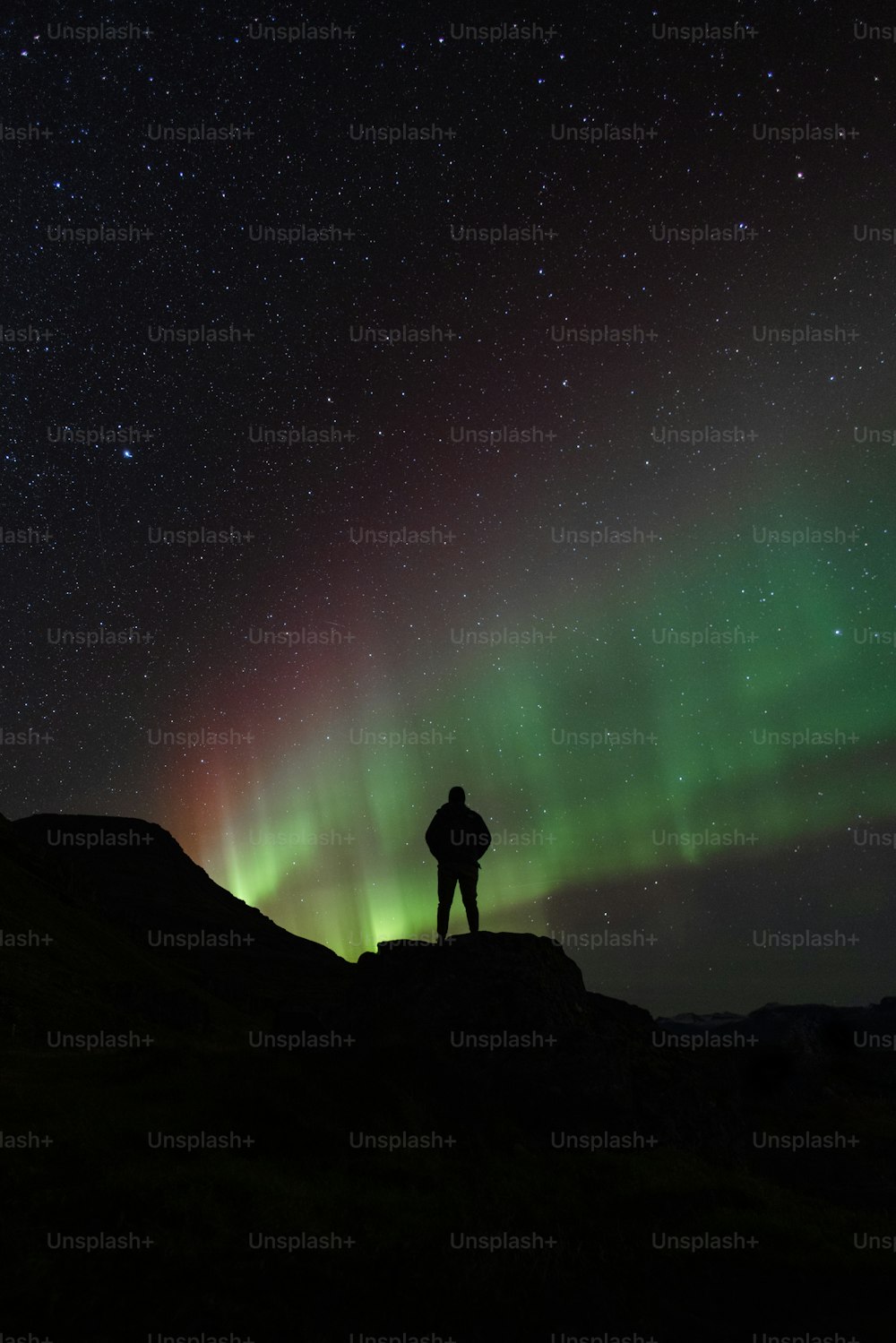 Una persona in piedi su una roccia che guarda l'aurora boreale nel cielo