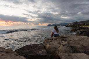 una persona seduta su una roccia vicino all'acqua