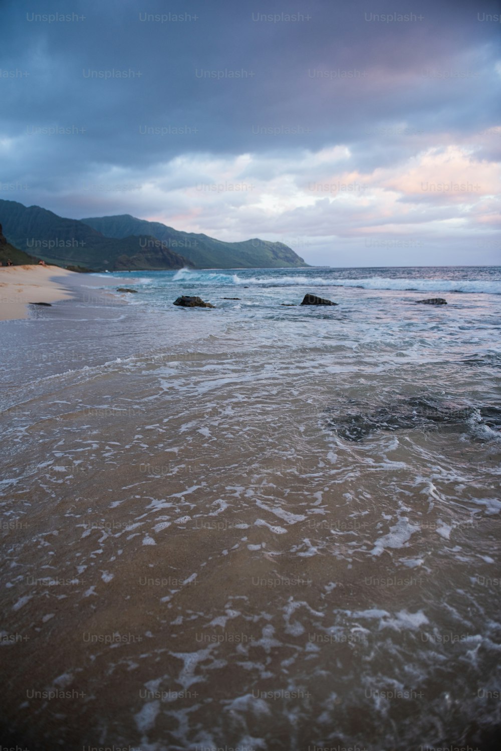 a body of water with waves and a beach with hills in the background