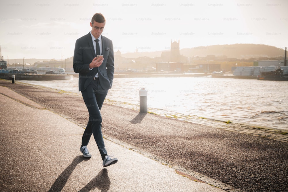 Un uomo in giacca e cravatta che cammina su un marciapiede vicino a uno specchio d'acqua
