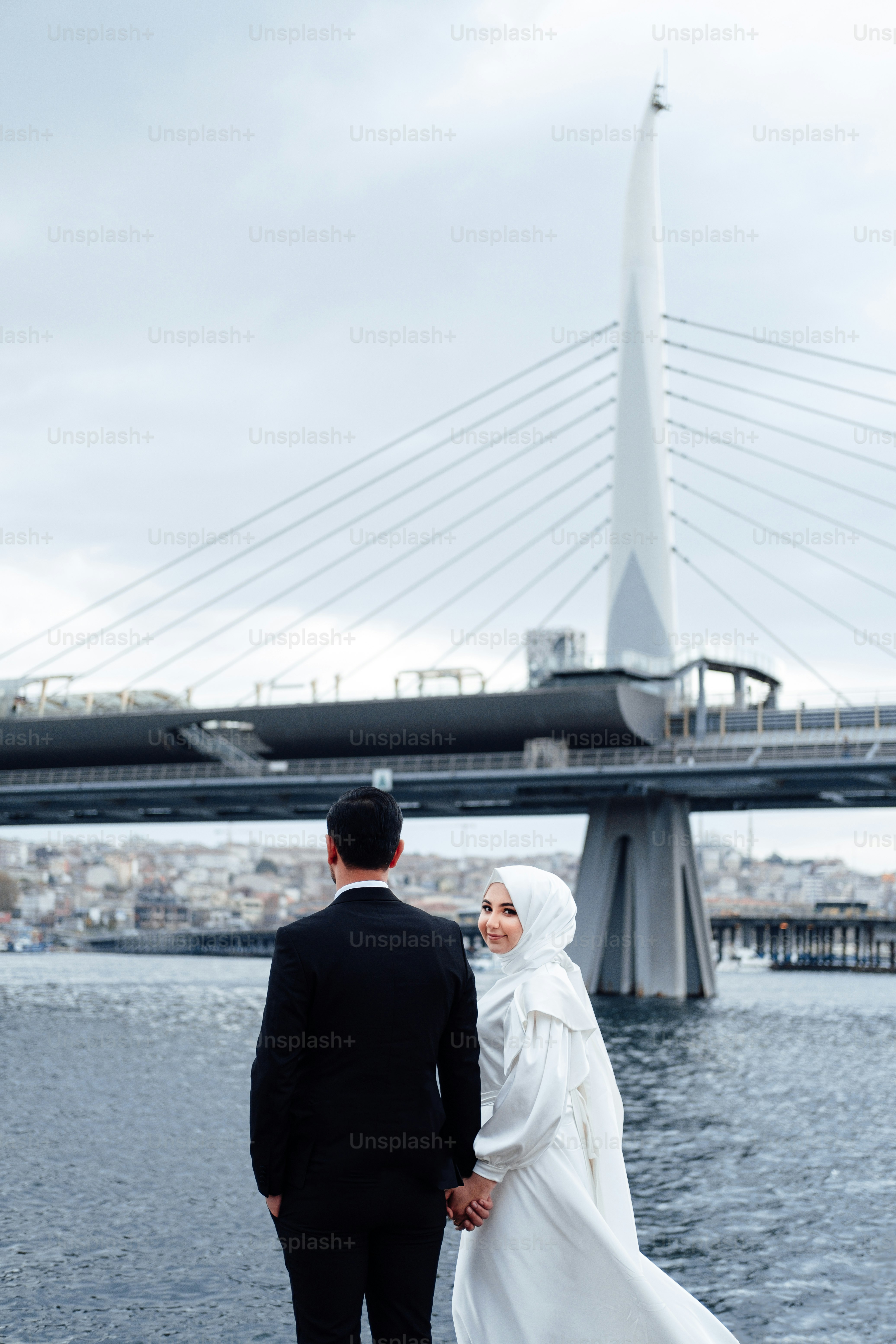 a man and woman walking on a bridge with a large bridge in the background