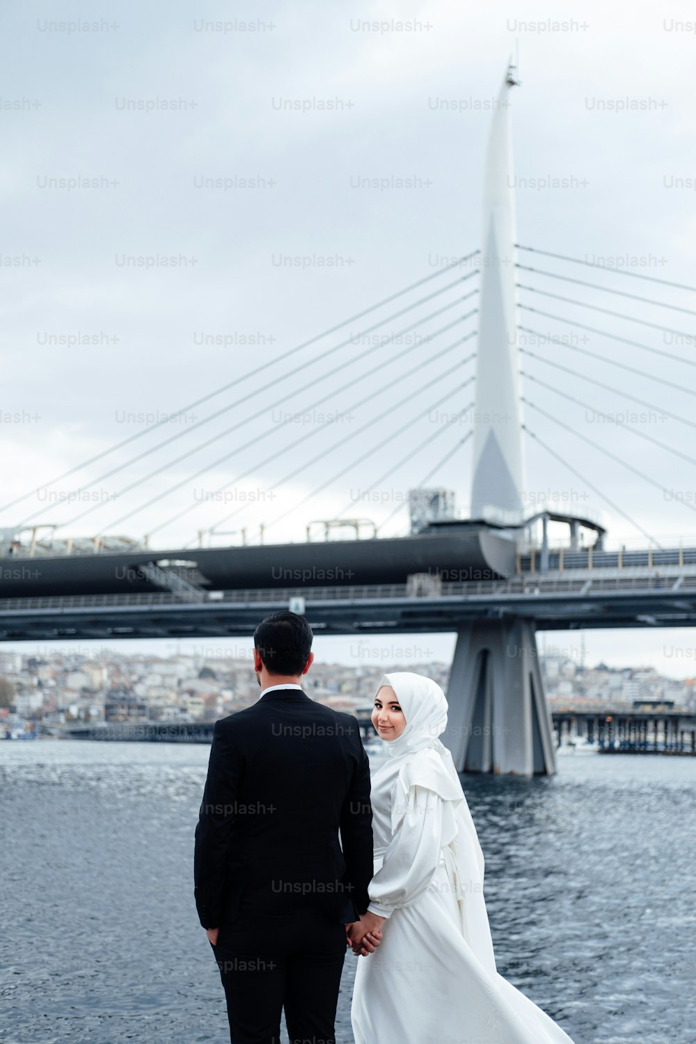 a man and woman walking on a bridge with a large bridge in the background