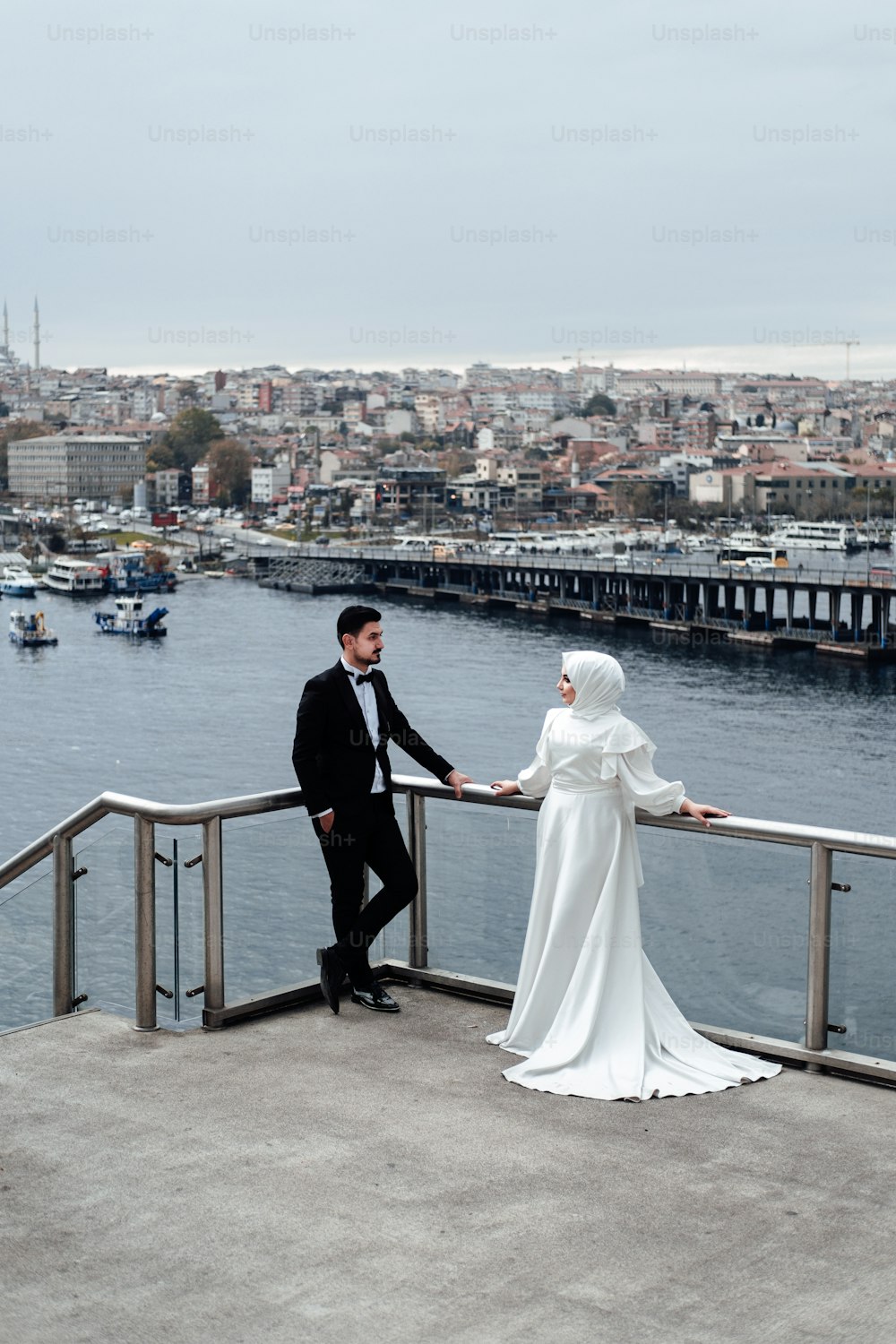 um homem e uma mulher em traje de casamento em pé em uma ponte sobre a água