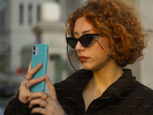 a person with red hair and sunglasses holding a cell phone