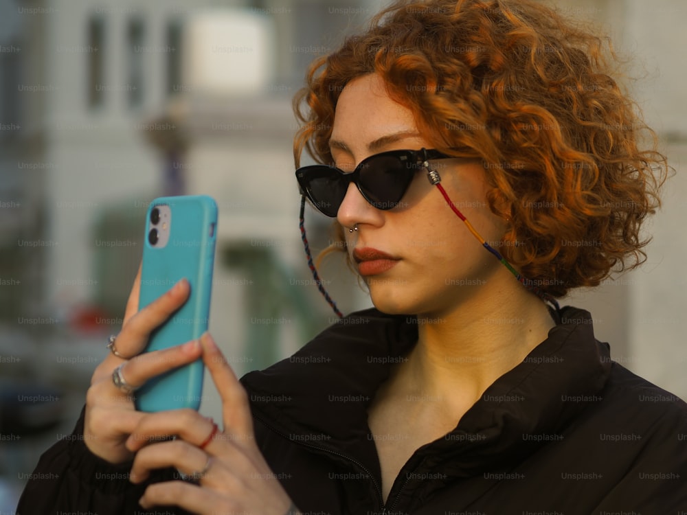 uma pessoa com cabelos ruivos e óculos escuros segurando um telefone celular
