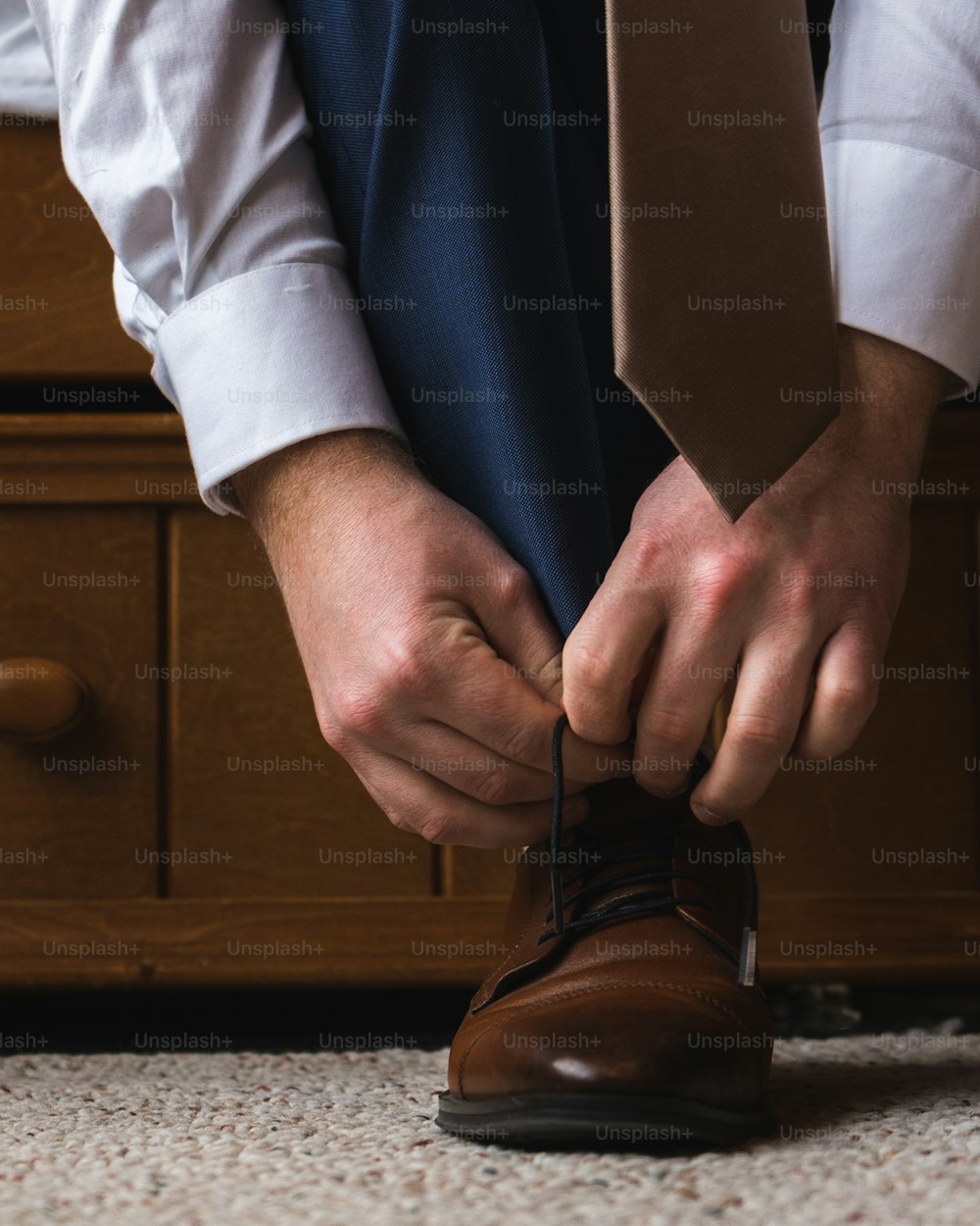 um homem amarrando uma gravata em um sapato marrom