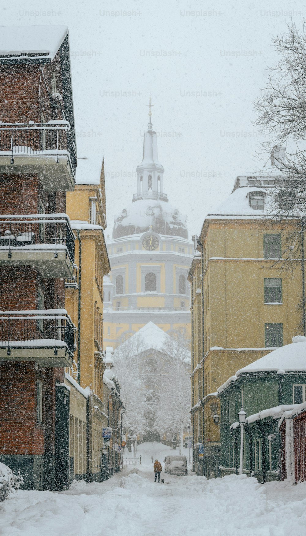 uma rua nevada com edifícios e uma torre à distância