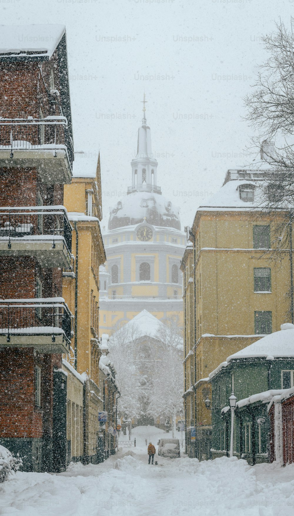 a snowy street with buildings and a tower in the distance