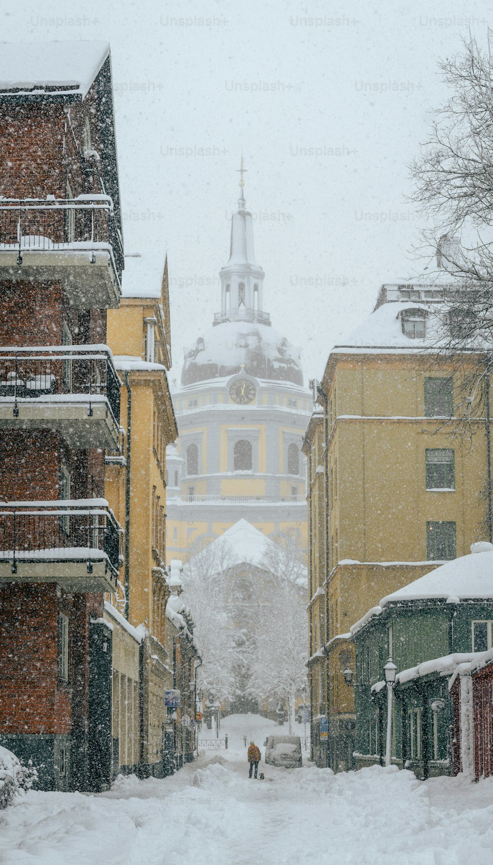 Una strada innevata con edifici e una torre in lontananza