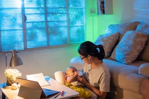 Asiatische Mutter und Kind Die Mutter sitzt und arbeitet nachts zu Hause und füttert das Baby.