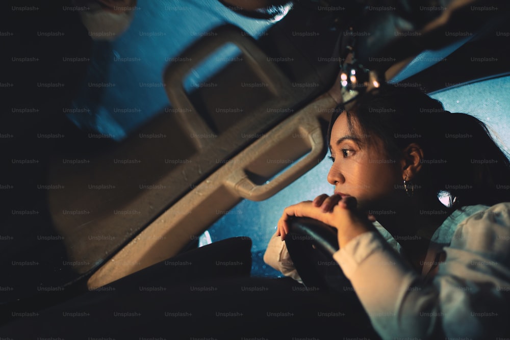 アジア人女性は夜に一人で運転している。雨が降っています。彼女は孤独です。