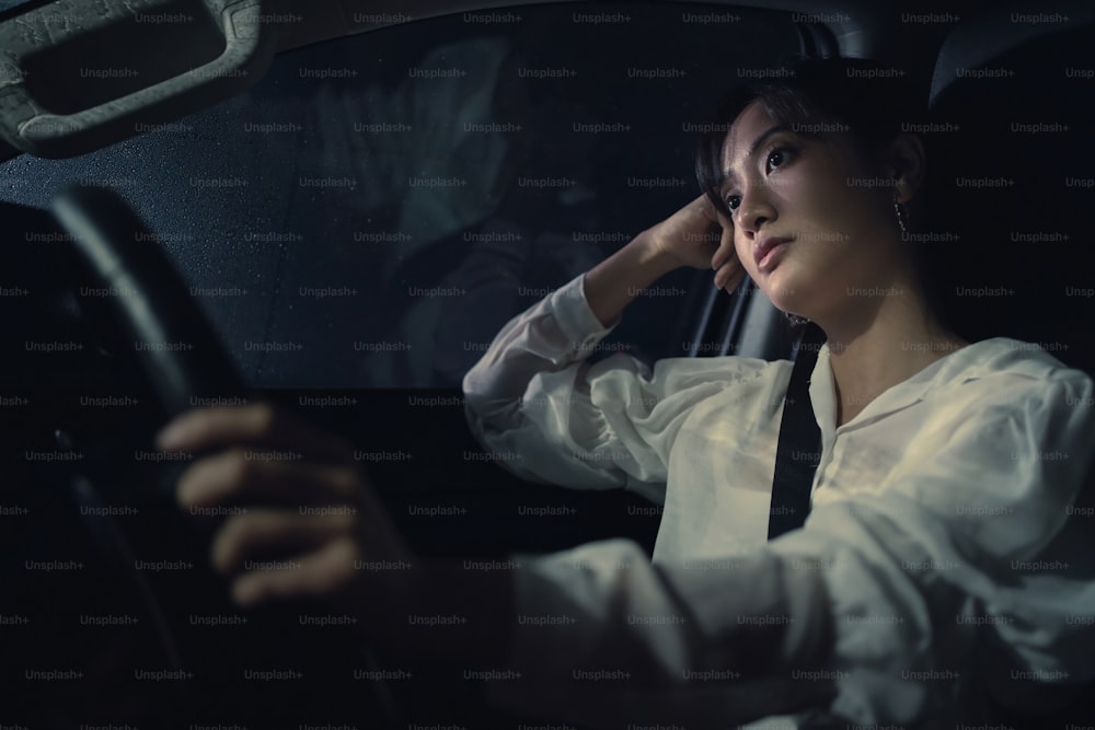 Una donna asiatica sta guidando da sola nella notte. Piove. È stressata.