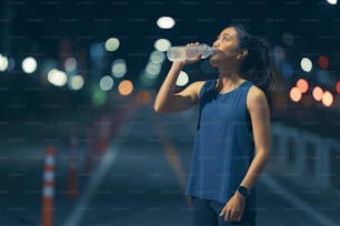 運動して走っているアジア人女性は、水を飲んでいる。