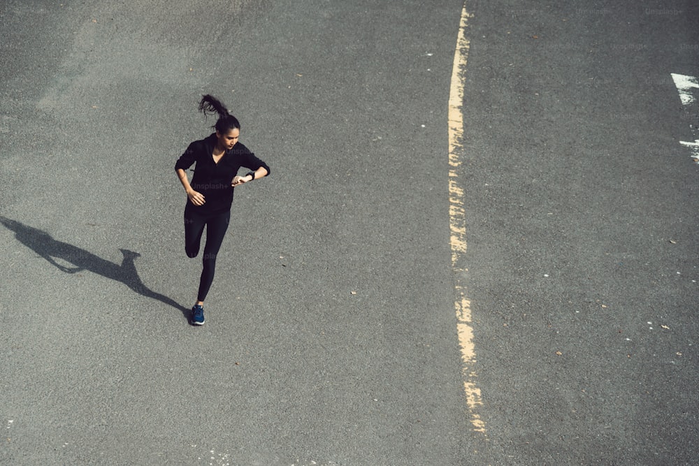 Mujer fitness que está corriendo el camino Ella mira la velocidad del reloj de pulsera.