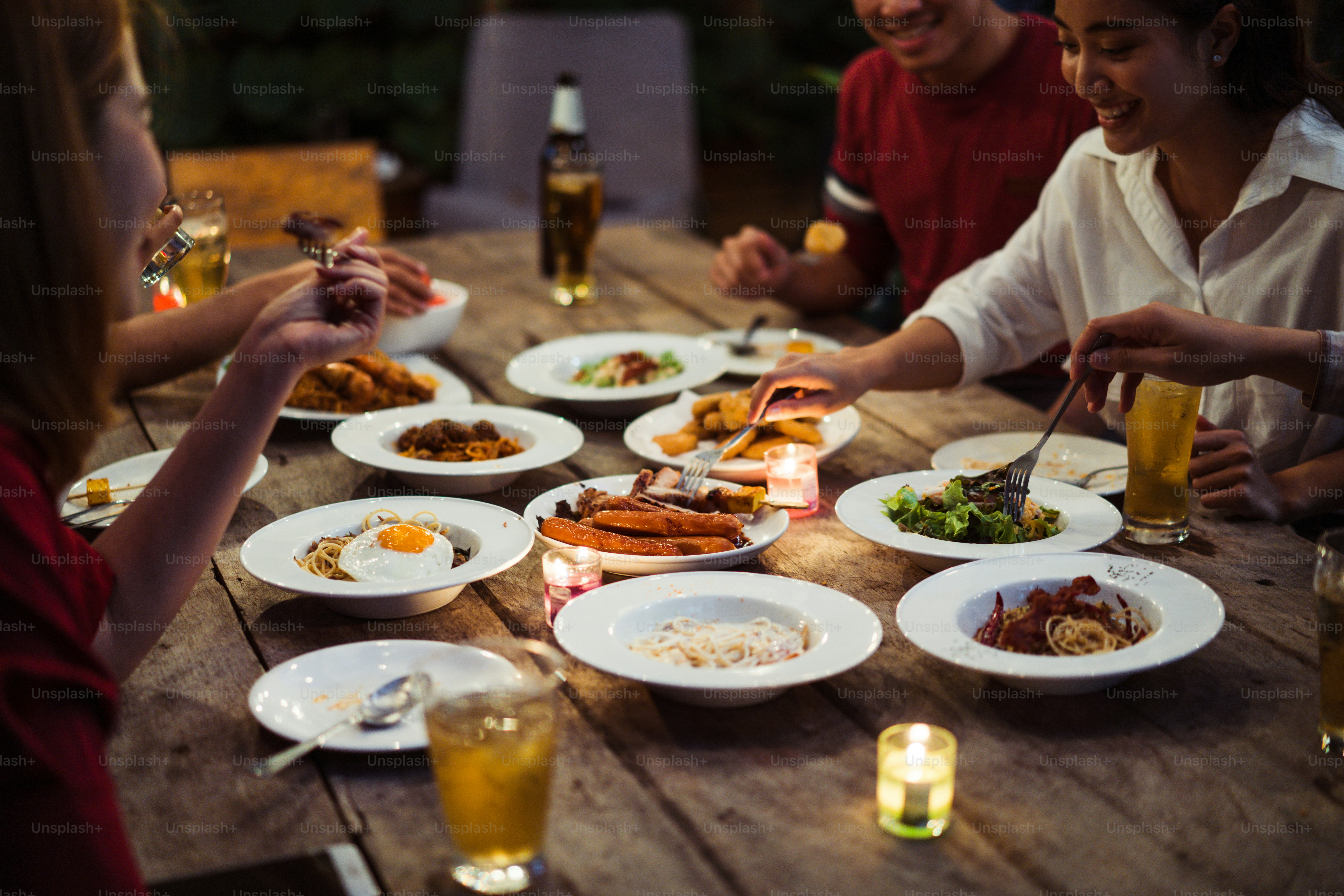 Asian group eating and drinking cold beer outside the house at night, having fun talking