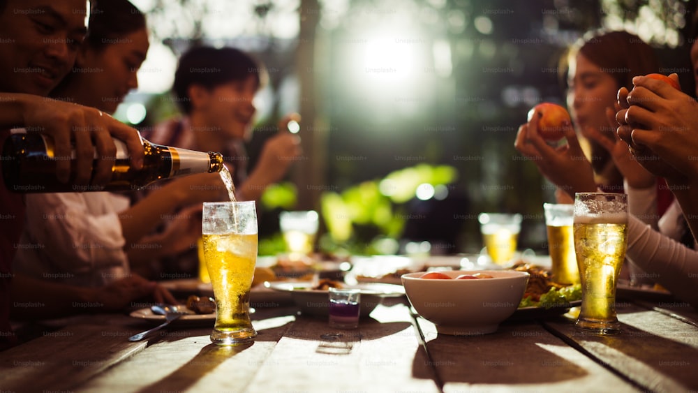 Grupo asiático comendo e bebendo cerveja gelada fora de casa à noite, se divertindo conversando
