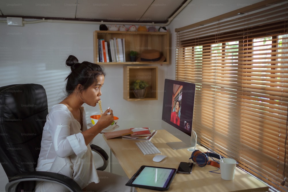 Donna asiatica Lavora a casa Sta mangiando spaghetti istantanei e videochiamate con il team.