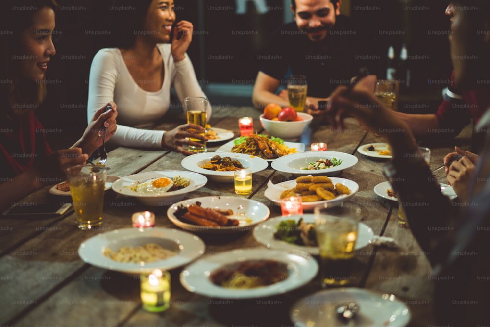 Asian group eating and drinking cold beer outside the house at night, having fun talking